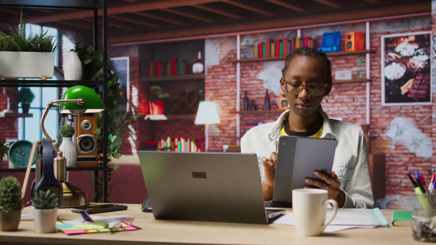 Woman at home taking break from work to look at social media feed on tablet. Remote employee at work in apartment office pausing tasks to use social network application on device, camera A