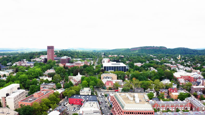 Aerial fly-in over New Haven, Connecticut, highlighting its iconic architecture, lush greenery, and the picturesque backdrop of rolling hills.