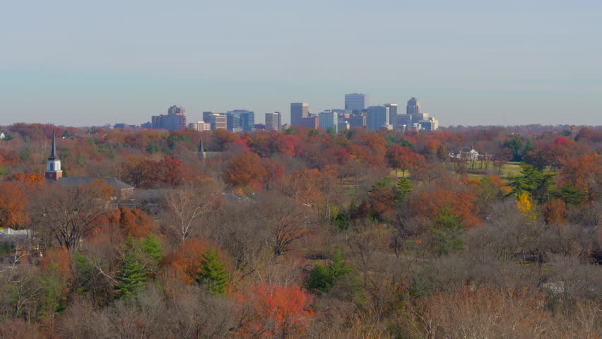 Stunning aerial rising over vibrant autumn trees and a charming church in St. Louis, Missouri. Features the downtown Clayton skyline on the horizon. Serene suburban beauty with urban sophistication.