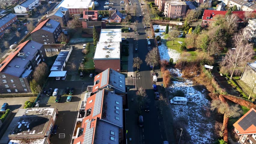 Cold and frosty winter day with sunlight in german neighborhood. Dripping cars in street. Solar panels on houses. Aerial top down flyover.