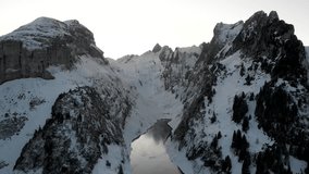 Aerial pan down view on a freezing lake Fälensee surrounded by snow and cliffs in Appenzell, Switzerland with a reflection of the winter sunset glow and mountain peaks on the dark ice - Powered by Shutterstock - Get 15% off with code: PIKWIZARD15