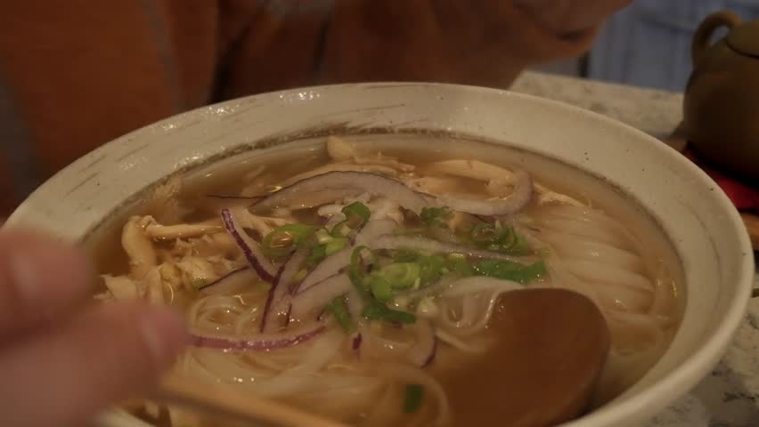 A warm bowl of Vietnamese chicken noodle soup with lime and fresh herbs being garnished