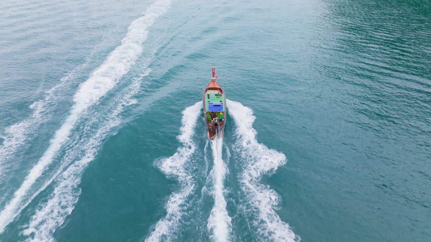This stunning aerial photograph depicts a longtail boat gracefully gliding through the tranquil and serene waters of Krabi, Thailand, perfectly capturing the essence of a tropical paradise
