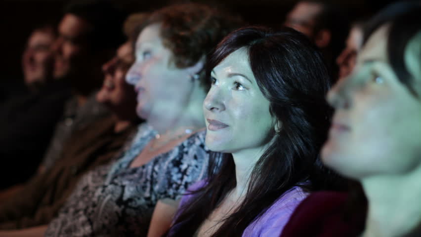 Attractive young woman watches a movie. Focus on her with a small dolly move and