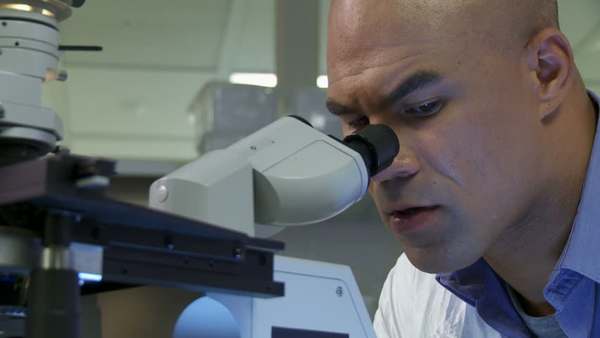 Scientist does research looking through a microscope in laboratory. Close up