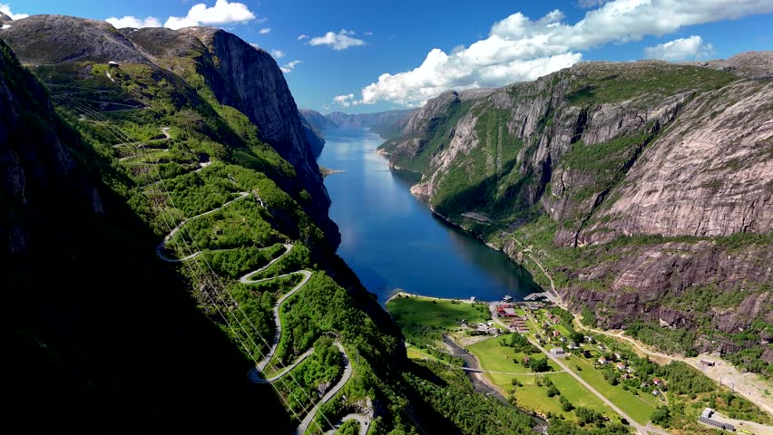 Majestic cliffs rise along the serene waters of Norways fjords, showcasing lush greenery and captivating winding roads. Lysefjord Lysebotn Norway