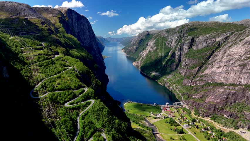 Majestic cliffs rise along the serene waters of Norways fjords, showcasing lush greenery and captivating winding roads. Lysefjord Lysebotn Norway