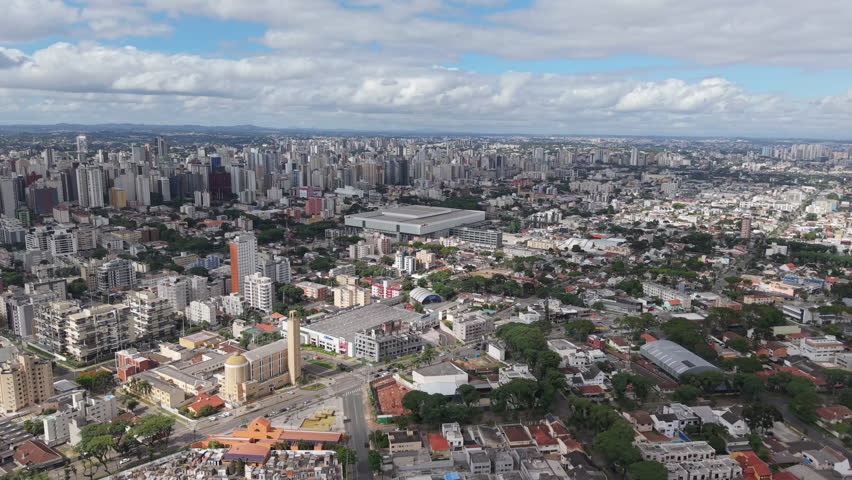 Panoramic aerial view of Curitiba, Paraná, Brazil, with the Ligga Arena stadium prominently in the center of the cityscape.