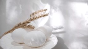 Easter decorations, white eggs and dry flowers, copy space. Easter still life. Sunlight and moving curtain shadows on white wall. Cozy home. Happy Easter background. - Powered by Shutterstock - Get 15% off with code: PIKWIZARD15