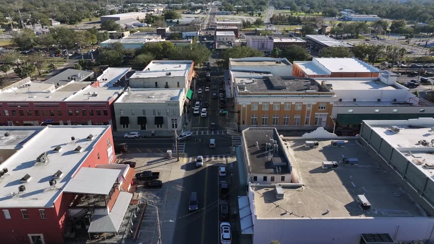 Junction with driving cars in historic small town of Plant City. Historic downtown in Florida during summer season. Main street and green trees with colored architecture buildings. Descend drone shot.
