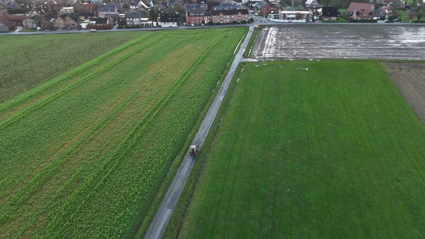 Tractor on path on agricultural farm fields in winter. Rainy day in american suburb. Top down shot. Aerial tracking shot.