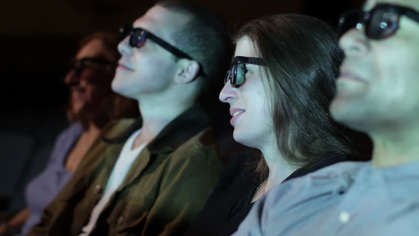 Young woman applauds as she watches a 3D movie. Focus on her with a small dolly