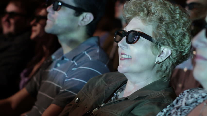Mature woman gets excited as she watches a 3D movie. Focus on her with a small