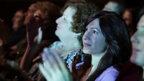 Attractive young woman applauds a movie. Focus on her with a small dolly move and projections on her face.