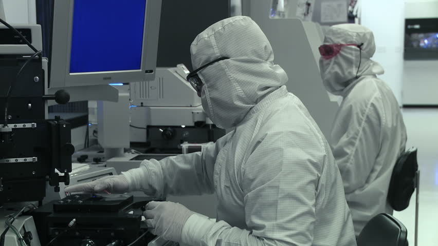 Two technicians working on silicon chip manufacture in a clean room, wearing