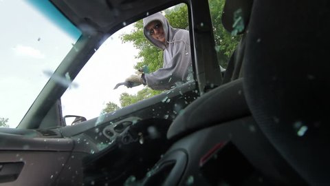 Burglar smashes a car window with a pry bar and reaches in to grab a bag with a laptop computer. Recorded with high shutter speed.