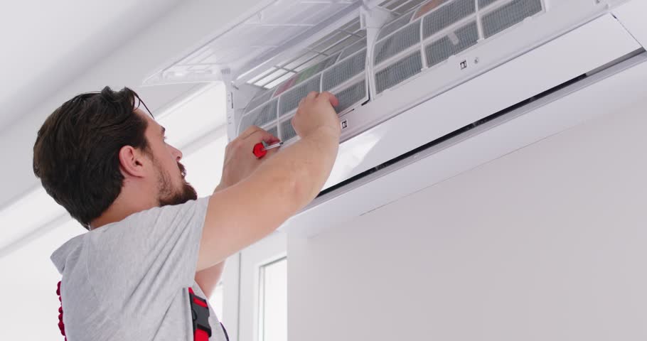 Close up of professional electrician or technician in work uniform removing air filter of modern air conditioner for cleaning or repairing, using screwdriver. Technician maintenance of cooling system.