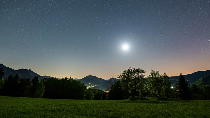 Star in Starry night sky moving over countryside nature at full moon Astronomy time lapse Night to day
