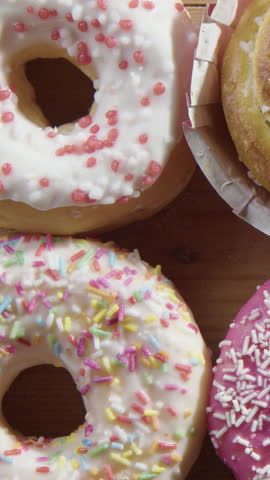 Vertical closeup slider over tasty donuts as hand chooses pink one