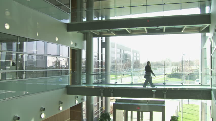 Backlit businessman and woman cross a walkway in a modern building atrium
