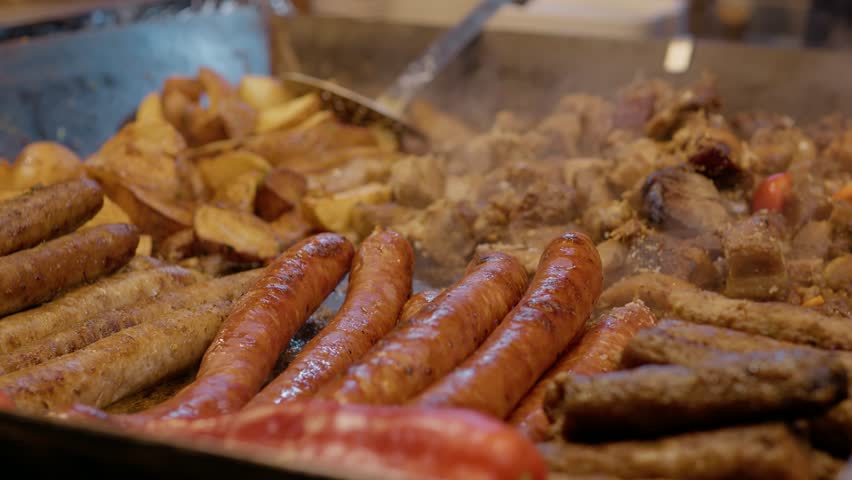 Street food vendor grilling sausages and potatoes on large hot plate, showcasing traditional outdoor culinary experience in bustling urban market setting