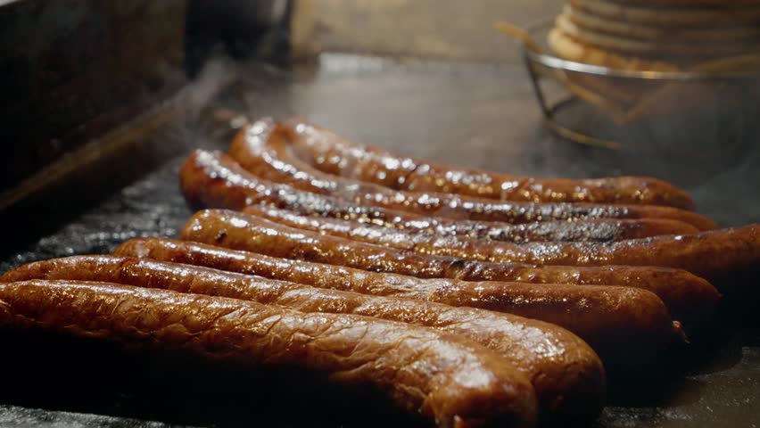 Sizzling sausages grilling on hot plate, releasing smoky aroma and appetizing golden brown crust while cooking over intense heat