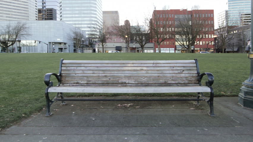Young couple talk and embrace on a park bench. Wide shot with the city of Portland, Oregon in the background.