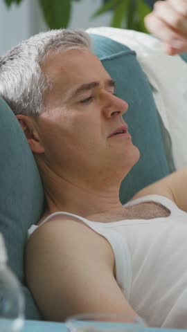 Exhausted man sitting on the couch at home during the summer heatwave, he is suffering from the heat