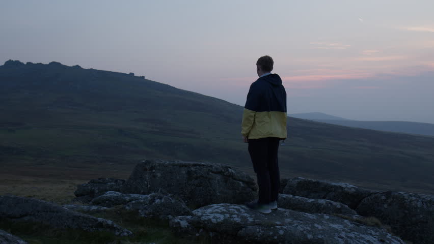 Dartmoor, Devon, England, UK, A Man Stands Atop a Rocky Hill, Gazing Out at the Serene, Expansive Landscape Bathed in the Warm Hues of Sunset, Medium Shot