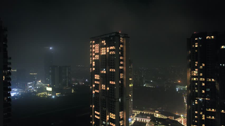 Aerial drone night shot flying between skyscrapers, homes, houses, office buildings covered in fog haze showing the cityscape and polluted winters of delhi, noida, gurgaon, bangalore