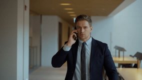 A serious businessman in his 30s picks up phone call while walking the office corridor - front view dolly pull back - Powered by Shutterstock - Get 15% off with code: PIKWIZARD15