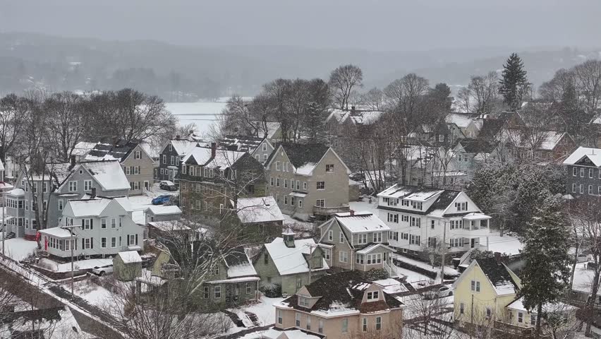 Colonial houses covered with snow in winter season. Houses and homes in small american town during winter snowstorm. Aerial descend wide shot.