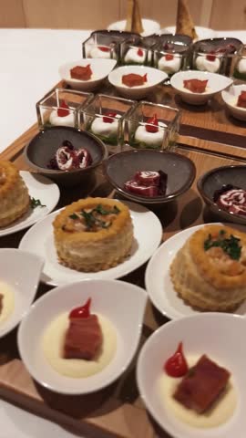 Gourmet appetizers presented on a wooden tray. The selection includes bite-sized savory pastries, creamy dips, and elegant bowls of artistic hors d’oeuvres. fine dining, culinary arts, catering