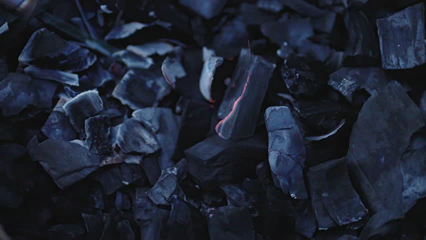 A closeup view of glowing charcoal pieces set against a dark background, beautifully showcasing their texture and heat