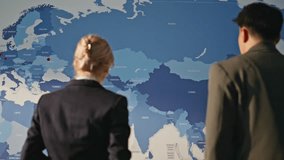 Businesspeople discussing global economy watching estimating map. Innovative team comparing business scopes over world at modern office. Two colleagues planning future ventures standing at cabinet  - Powered by Shutterstock - Get 15% off with code: PIKWIZARD15