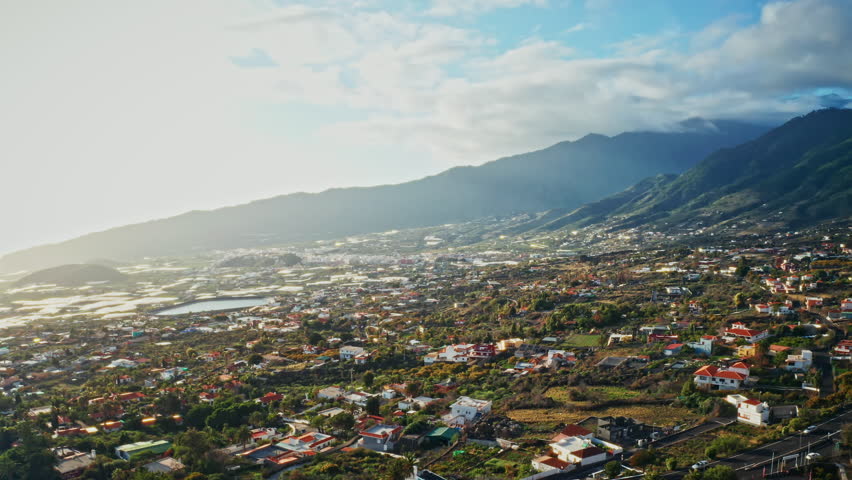 Aerial drone shot of the beautiful landscape in La Palma, Canary Islands, Spain. High view of the small local towns, the green lush vegetation and the majestic mountains in the background.