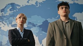 Two business analysts posing in blue world map background portrait. Confident global market team looking camera at modern cabinet room closeup. Serious colleagues couple standing together zoom out  - Powered by Shutterstock - Get 15% off with code: PIKWIZARD15