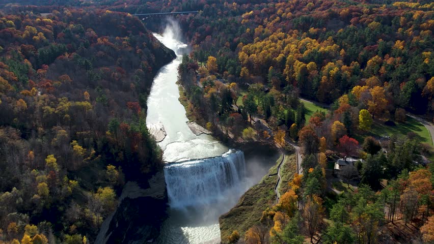 An aerial view of a stunning waterfall surrounded by vibrant autumn foliage, flowing into a river in a serene natural landscape