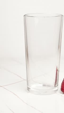 Vertical screen: natural milk yogurt with strawberries pouring into glass cup on white background. Dairy products with addition of wild berries. Isolated