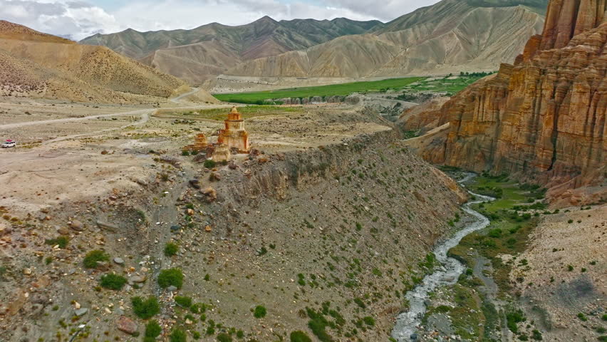 A weathered stupa stands resilient amidst the eroded, rugged terrain of Nepal, showcasing the harmony between ancient architecture and nature