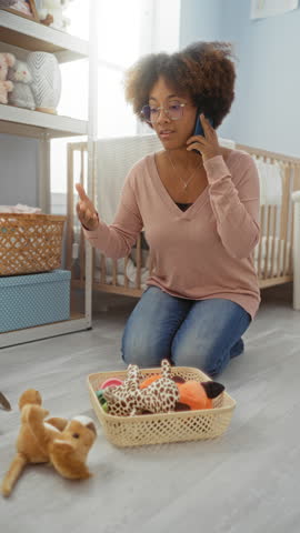 Woman talking on phone in bedroom while arranging toys, showing calm interaction in cozy home environment with soft lighting and curly hair style.