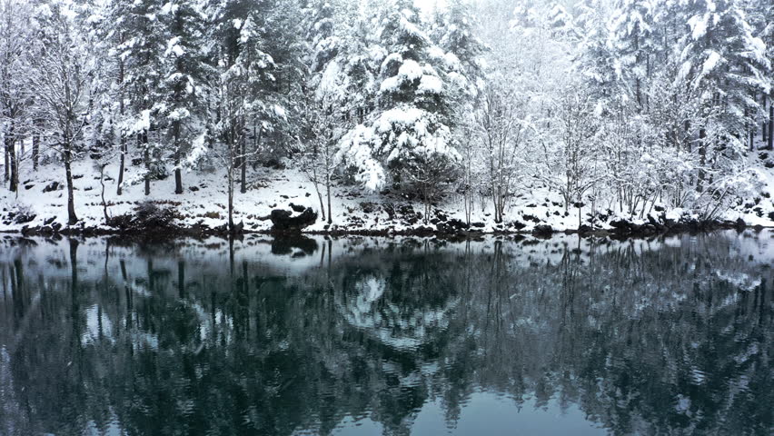 A serene snowy forest reflected in a calm lake, evoking peace and solitude