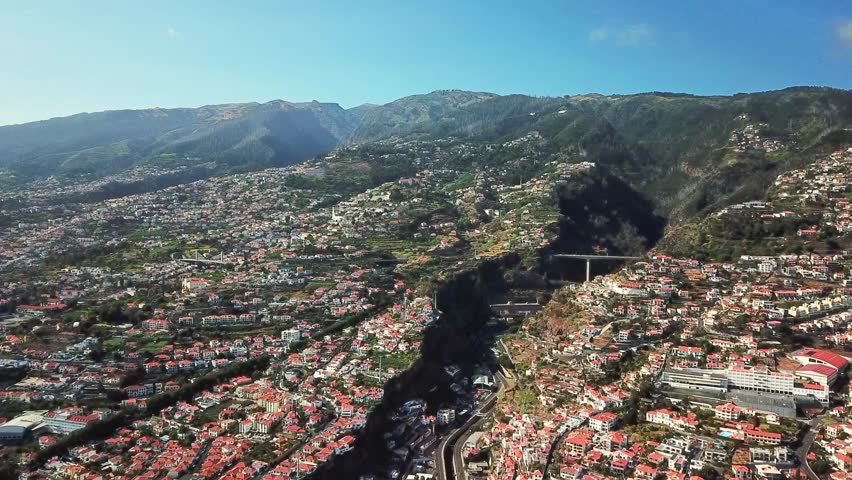 A stunning aerial view of Funchal Madeira, showcasing its vibrant cityscape, terracotta rooftops, and lush mountainous backdrop, highlighting its unique landscape and urban charm