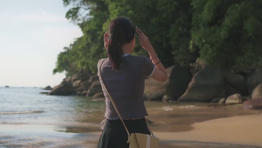 Happy adorable girl in casual dress relaxing on the beach under sunlight. Attractive carefree female teenager enjoy on the coastal area. Outdoor pursuit.