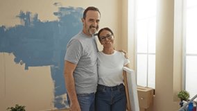 Middle-aged hispanic couple embraces in a new home living room, surrounded by boxes, expressing love and satisfaction after finishing an interior painting project together. - Powered by Shutterstock - Get 15% off with code: PIKWIZARD15