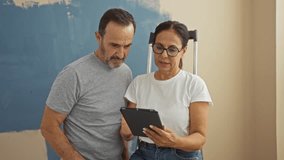 Middle-aged hispanic couple enjoying time indoors in a new home while using a tablet together in their living room with love and family bonding. - Powered by Shutterstock - Get 15% off with code: PIKWIZARD15