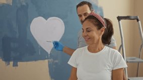 Hispanic couple embraces lovingly in a newly painted living room, with a heart on the wall and a ladder nearby, capturing warmth, joy, and togetherness in their shared home project. - Powered by Shutterstock - Get 15% off with code: PIKWIZARD15