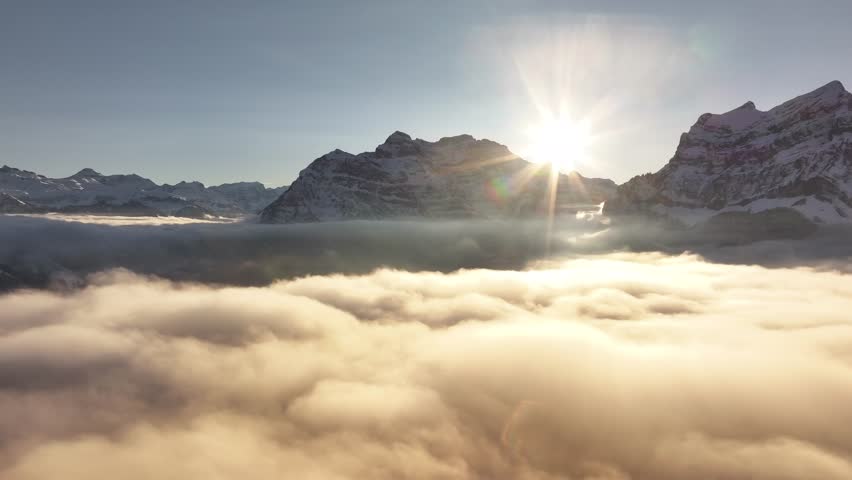 Stunning aerial drone view of sunrise over Swiss alps with Rautispitz and Glärnisch peaks rising above blanket of clouds, breathtaking natural landscape.