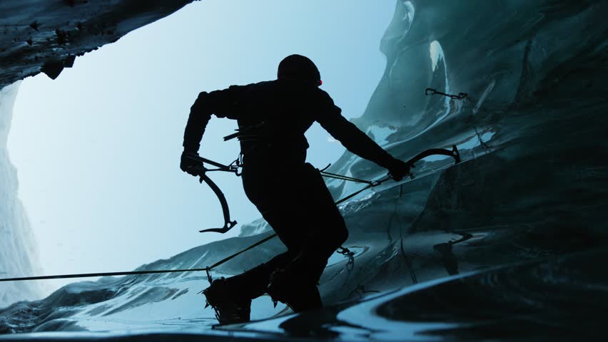 Man climbing frozen ice cave in winter mountains