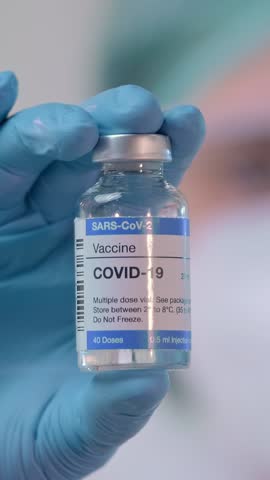 Healthcare professional in gloves showcases a covid-19 vaccine vial, emphasizing the importance of vaccinations for public health in a clinical environment.